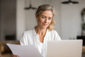 Person i 40-årsåldern vid skrivbord med laptop och anteckningar